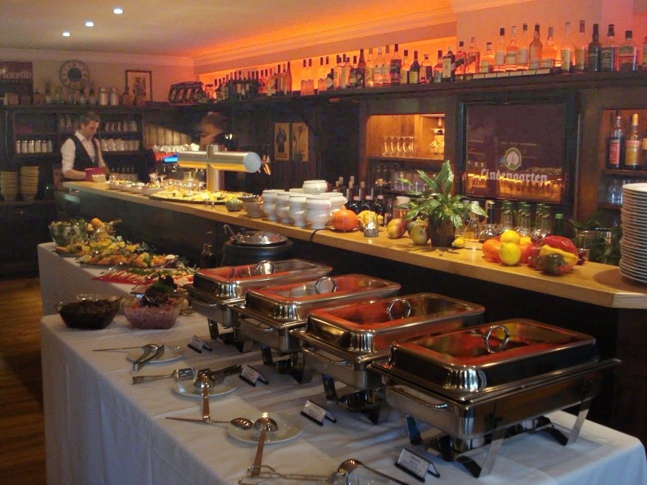 Buffet mit kalten Platten und warmen Speisen vor der aufgehellten Bar